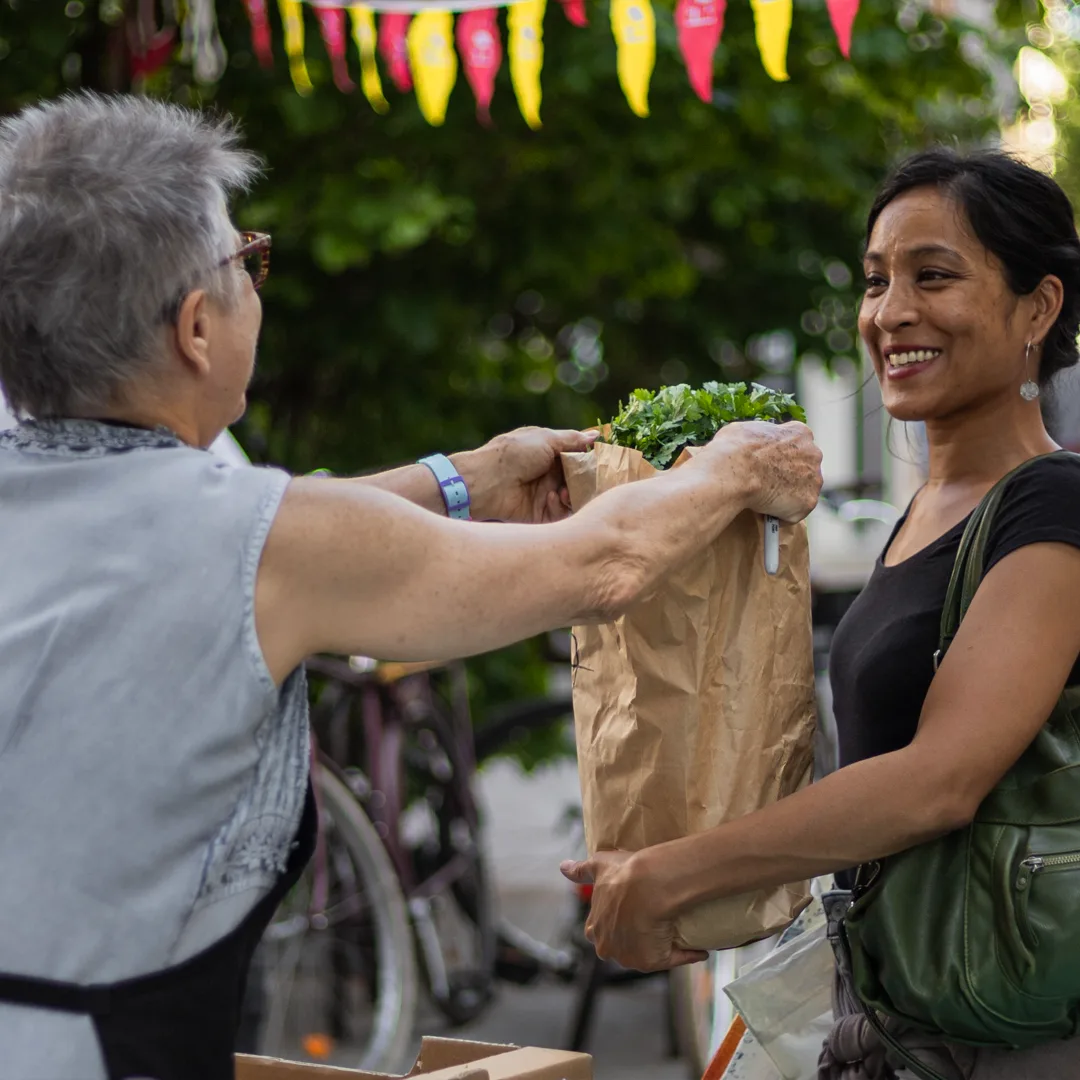 Une bénévole remet un sac de légumes à une adhérente, en rue.