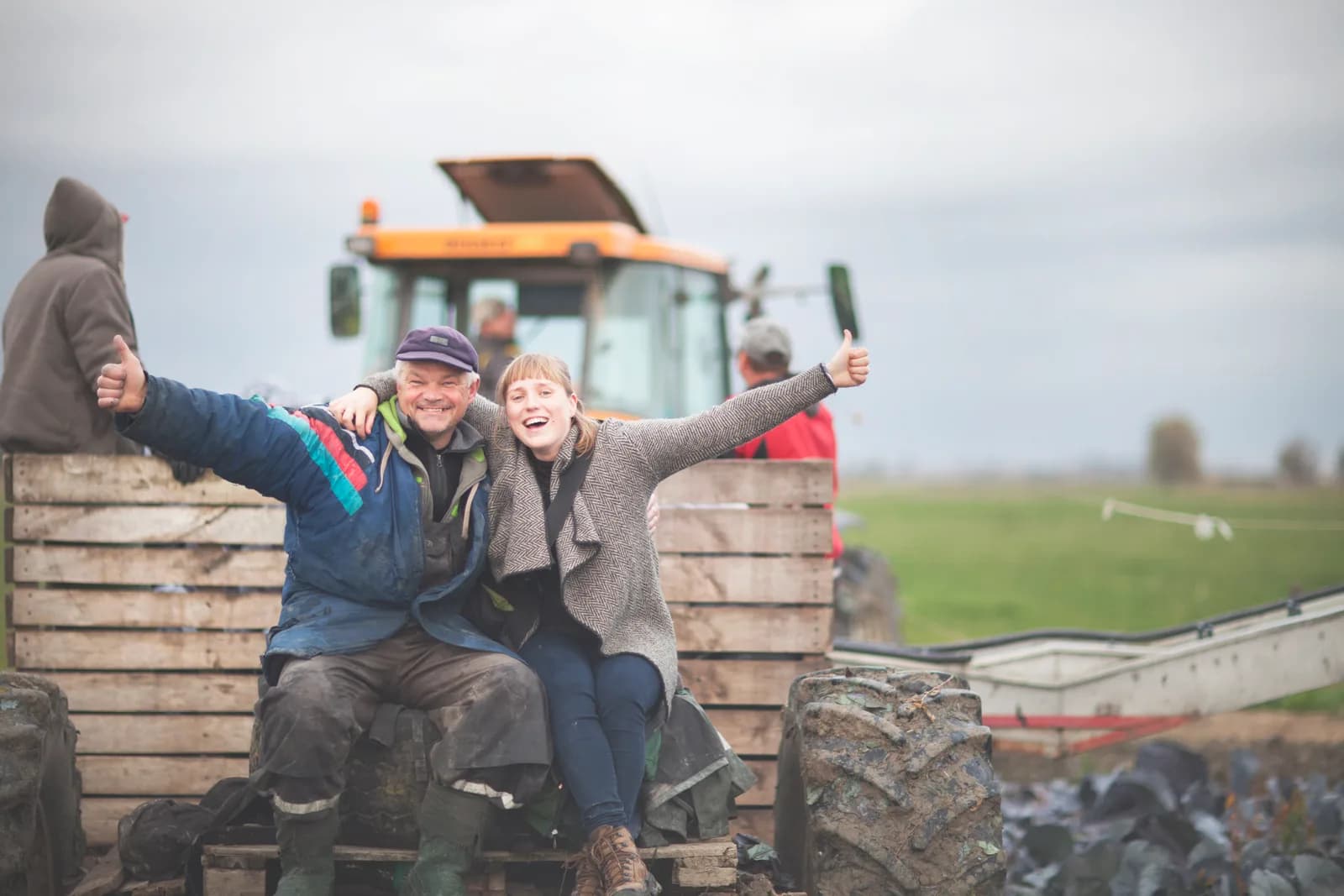 Trois personnes lèvent les bras, assises sur du matériel agricole dans un champ.