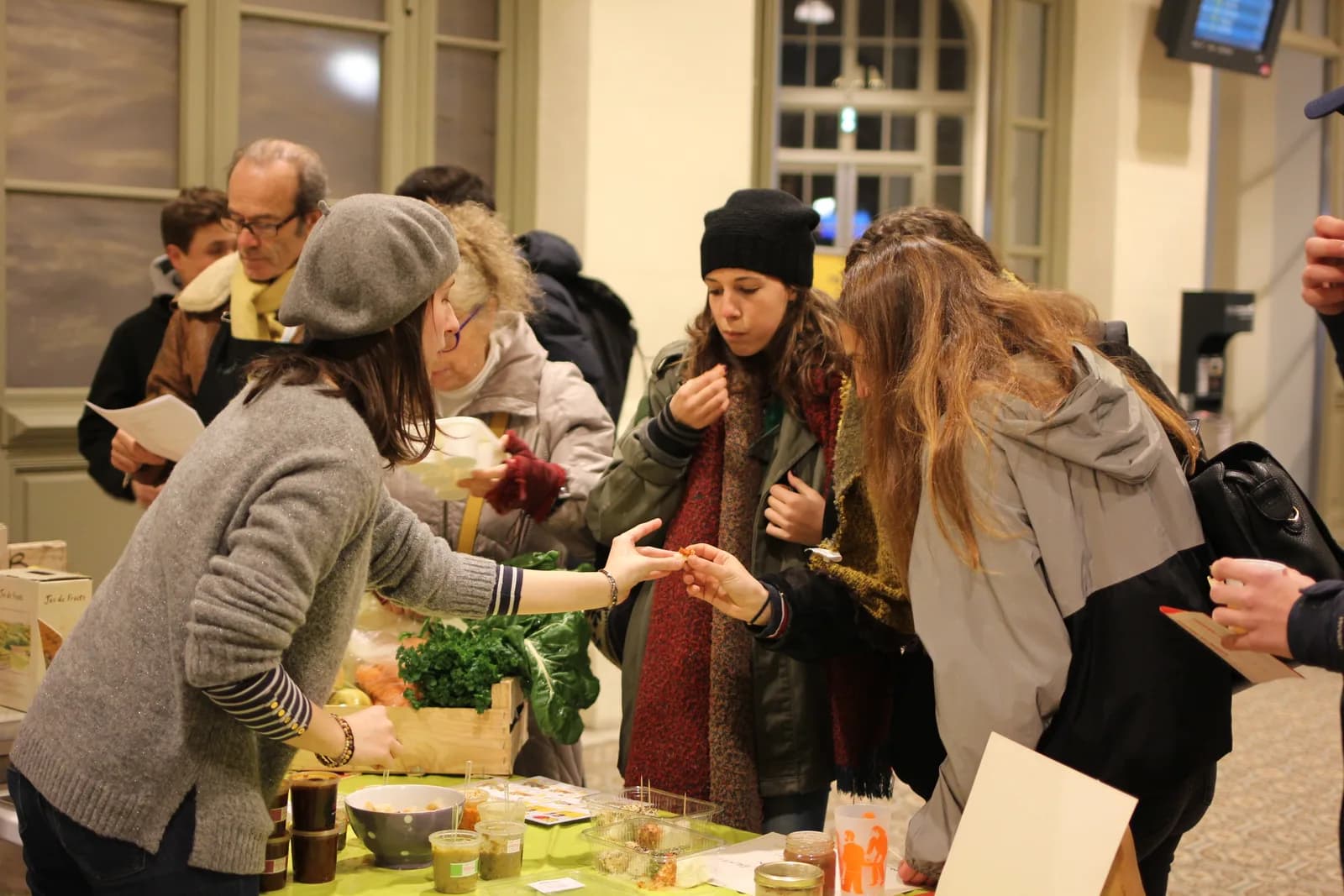 Un marché couvert, des personnes rassemblées autour de tables de produits.