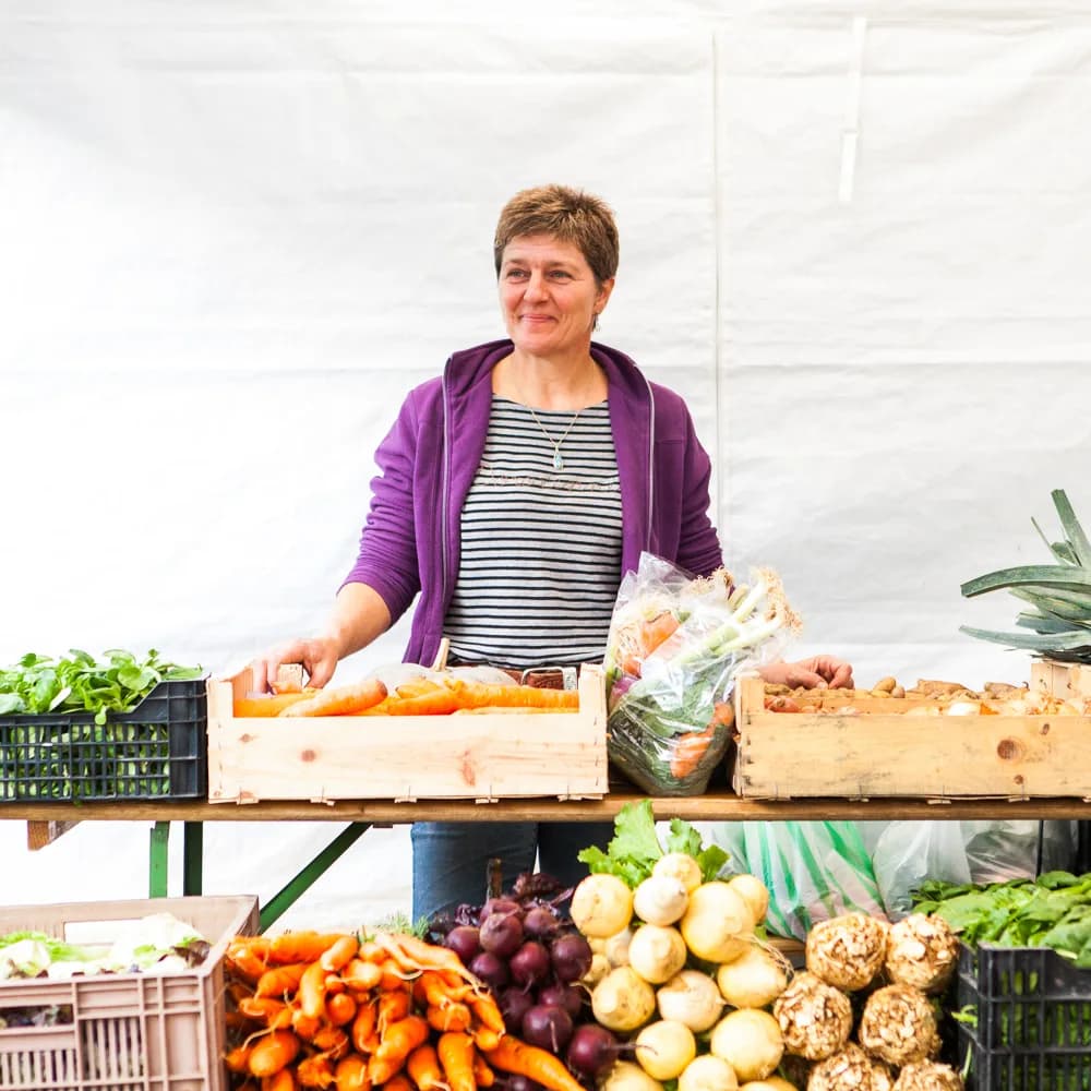 Une femme derrière un étal de légumes, au marché.