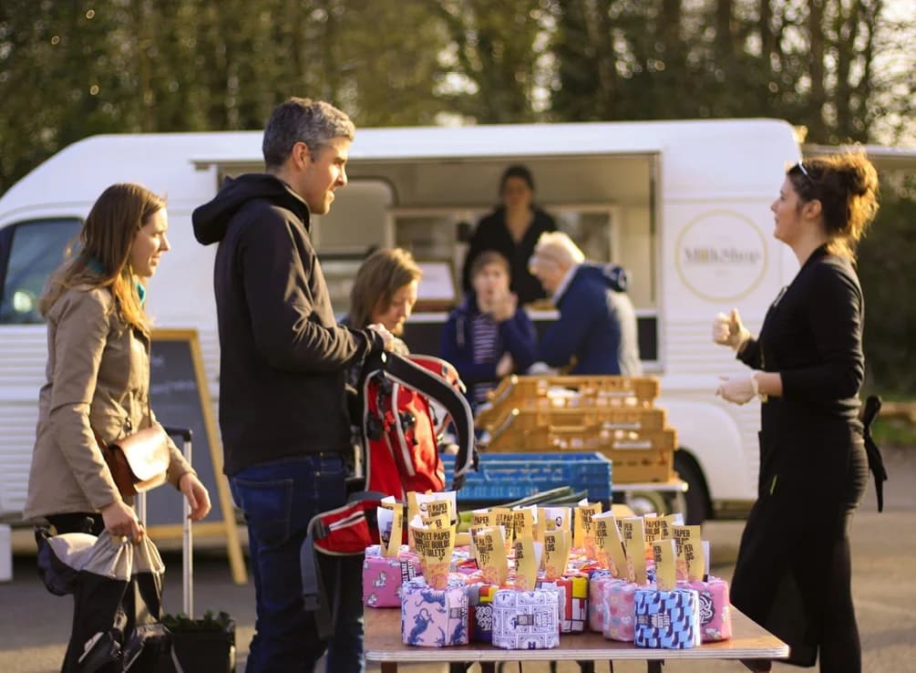 Un étal de distribution en fin de journée : cagettes, produits emballés et une camionnette de ferme.